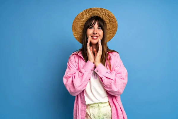 美しいブルネットの女性の夏の肖像画は スタジオブルーの背景にポーズを藁帽子と明るいリネンシャツを身に着けている 休暇のスタイル — ストック写真