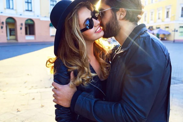 Style sexy couple amoureux embrasse dans la rue à la lumière du soleil du soir de la ville. porter des lunettes de soleil et costume glamour rock noir — Stockfoto