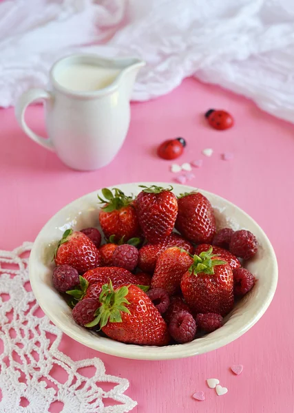 Fresas y frambuesas en un plato sobre fondo rosa — Foto de Stock