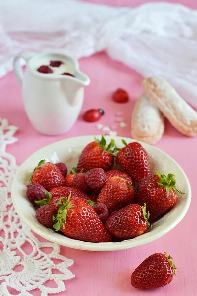 Fresas y frambuesas en un plato sobre fondo rosa — Foto de Stock