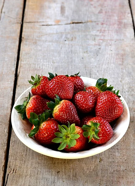 Fresas en un plato blanco sobre fondo de madera — Foto de Stock