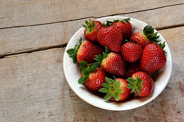 Fresas en un plato blanco sobre fondo de madera — Foto de Stock