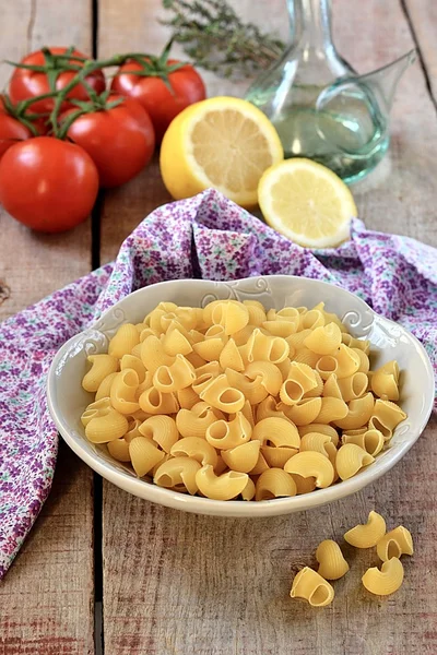 Pastas crudas en un bol con aceite de oliva, limón y tomates — Foto de Stock