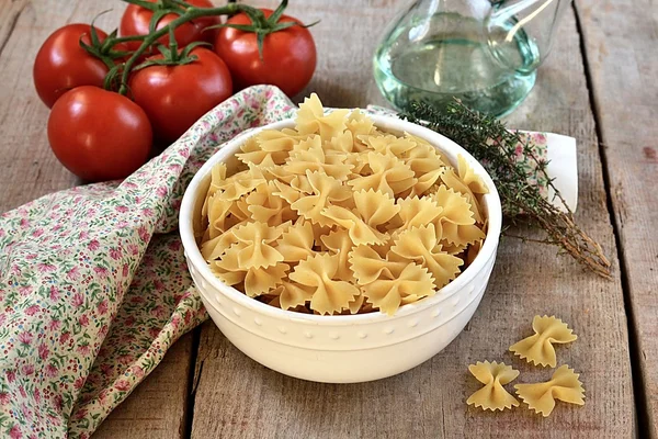 Ruwe pasta in een kom met olijfolie en tomaten — Stockfoto