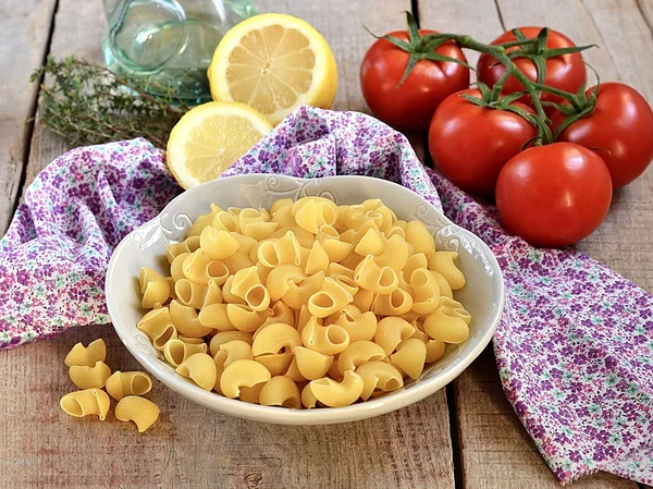 Ruwe pasta in een kom met olijfolie, citroen en tomaten — Stockfoto
