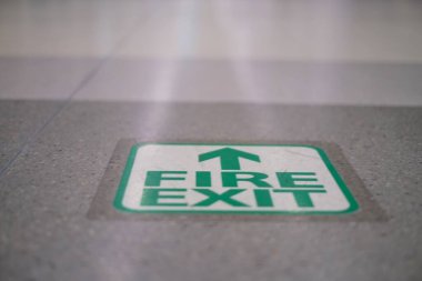 Yeşil bir yangın çıkışı, gri fayans zemininde bir okla, acil durum ya da yangın durumunda binanın dışındaki güvenli bölgeyi gösteriyor..