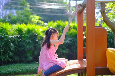 Yeşil çimenler, ağaçlar ve güneşli bir günde halka açık bir parkta ahşap merdiven tırmanan genç bir Asyalı kız..