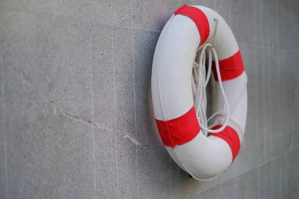 A red and white lifesaver with rope, hanging on a wall by a pool  for safety to rescue drowning swimmers.