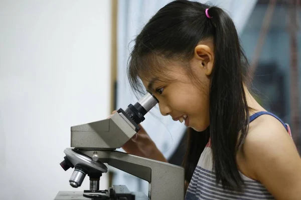 Genç ve tatlı bir Asyalı kız biyoloji laboratuvarında mikroskop kullanmayı öğreniyor. Eğleniyor, tek hücreli organizmaları inceliyor..