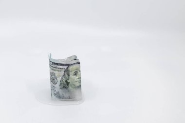 Yavaşça 100 dolarlık banknotları eritiyor. Beyaz arka plandaki buz küpünün içinde, fotokopi uzayı ile donduruluyor. Donmuş mal varlığı kavramı, dondurulmuş ekonomi, soğuk para veya yavaş ekonomi.