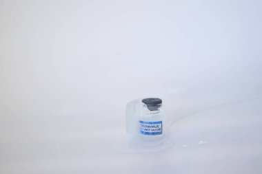 Corona virüsü aşısı için çok düşük depolama sıcaklıklarına sahip Corona virüsü aşısı olan Glass şişesinin içinde dondurulmuş COVID aşısıyla yavaş yavaş eriyen buz küpü. Beyaz arkaplan, alanı kopyala