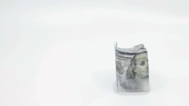 Yavaşça 100 dolarlık banknotları eritiyor. Beyaz arka plandaki buz küpünün içinde, fotokopi uzayı ile donduruluyor. Donmuş mal varlığı kavramı, dondurulmuş ekonomi, soğuk para veya yavaş ekonomi.