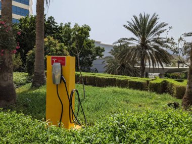 DUBAI, UAE - CIRCA 2021: Tesla Super Charger in the green area in front of a luxury hotel clipart