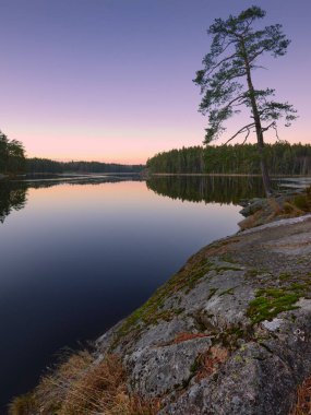 Granit taşlar, çam ağaçları ve orman Fin gölünün berrak sakin sularına yansımaktadır..