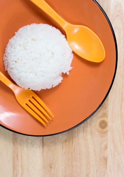 Ρύζι σε πορτοκαλί πιάτο με κουτάλι στο ξύλινο τραπέζι — Φωτογραφία Αρχείου