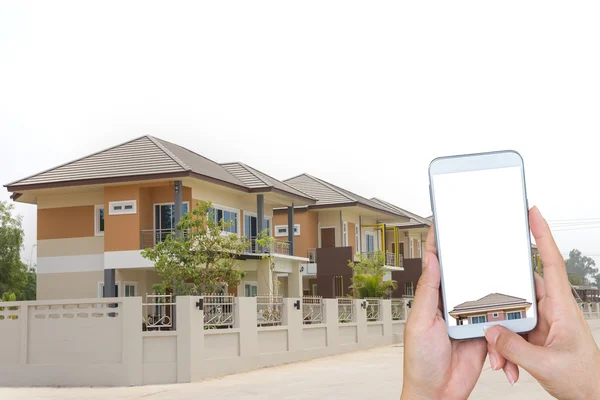 Mano sosteniendo un teléfono inteligente y una casa nueva . — Foto de Stock