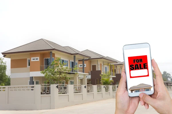 Mano sosteniendo un teléfono inteligente y una casa nueva . — Foto de Stock