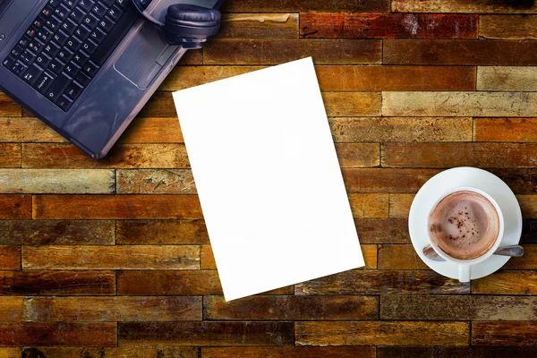 Un papel en blanco en la mesa de oficina de madera con ordenador portátil y una taza de coff — Foto de Stock