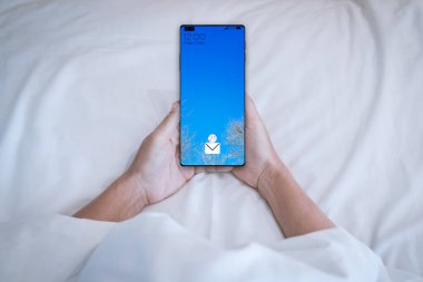 Yatakta uyanırken akıllı telefonunu tutan adam..