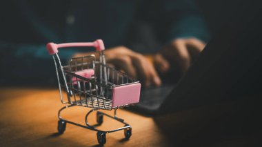 Laptop kullanan birinin alışveriş arabası masada. Çevrimiçi alışveriş kavramı, dijital pazar yeri, e-ticaret sitesi, ürün arama, çıkış süreci, perakende pazarlama, tüketici satın alma davranışı.