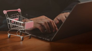 Laptop kullanan birinin alışveriş arabası masada. Çevrimiçi alışveriş kavramı, dijital pazar yeri, e-ticaret web sitesi, ürün arama, küçük işletme, perakende pazarlama, tüketici satın alma davranışı.