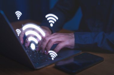 Kablosuz bağlantı, yüksek hızlı internet erişimi, dijital iletişim, ağ teknolojisi ve modern çevrimiçi çalışma ortamlarını sembolize eden bir dizüstü bilgisayar kullanan kişi.