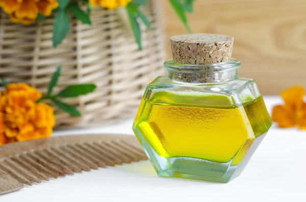 Small bottle of cosmetic oil with marigold flowers extract and wooden hair comb — Stock Photo, Image