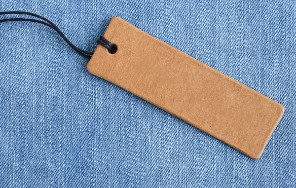 Blank paper label on a light blue denim fabric. Jeans background with sale or price tag.