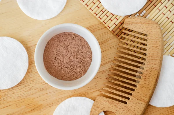 Pink bentonite clay powder in the small white bowl and hair brush. Clay texture close up. Diy facial or hair mask, dry shampoo recipe. Natural beauty treatment and spa. Top view, copy space