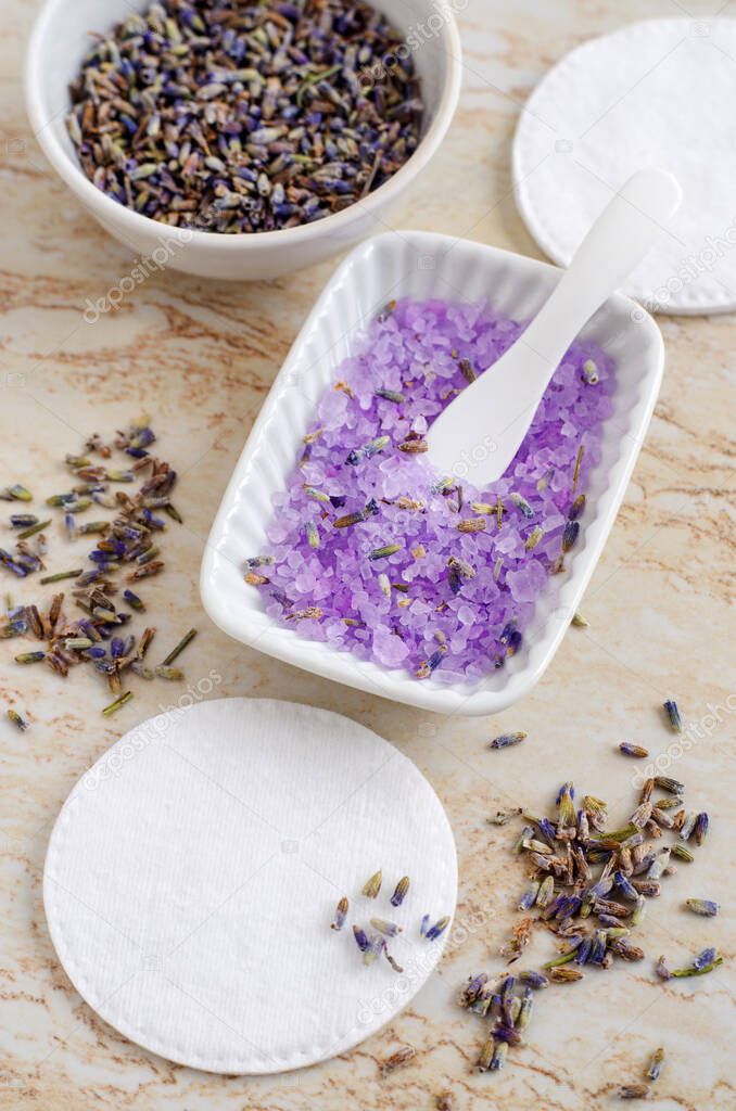 Small porcelain bowl with purple bath salts (foot soak), dry lavender flowers and cotton pads. Homemade spa and beauty recipe.
