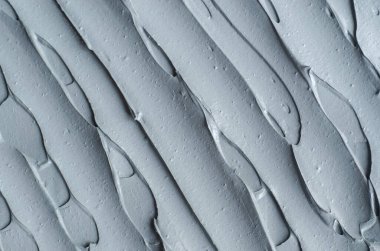 Gri bentonit yüz kilini (aljinat maskesi, yüz kremi, vücut sargısı) kapat, seçici odaklanma. Fırça darbeleriyle soyut arkaplan.  