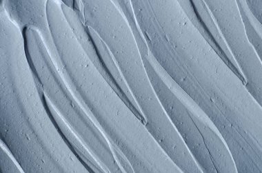 Gri bentonit yüz kilini (aljinat maskesi, yüz kremi, vücut sargısı) kapat, seçici odaklanma. Fırça darbeleriyle soyut arkaplan.  