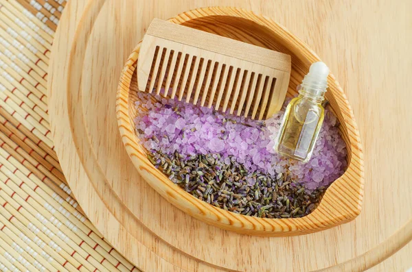 Wooden plate with dry lavender, purple bath salts (foot soak), wooden hair brush and bottle with esential oil. Homemade spa and beauty treatment concept. Flat lay
