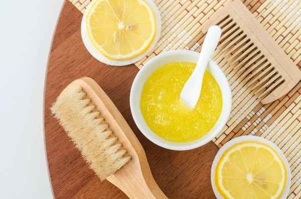 Homemade lemon fruit scrub (bath salt, foot soak, facial or hair mask) in a small white bowl and wooden hairbrush. Natural beauty treatment, hair care and spa recipe. Top view, copy space.