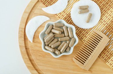 Yiyecek takviyeli kapsülleri ve ahşap saç fırçası olan küçük beyaz bir kase. Doğal sağlık, saç bakımı ve güzellik tedavisi. Üst görünüm, alanı kopyala.