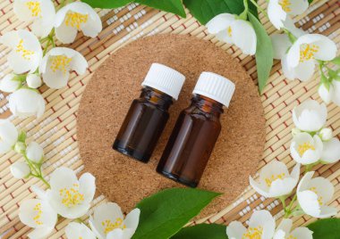 İki küçük cam şişe yasemin yağı (tentür, infüzyon, parfüm) ve yasemin çiçekleri. Aromaterapi, spa ve bitkisel ilaç malzemeleri. Üst görünüm, alanı kopyala. 