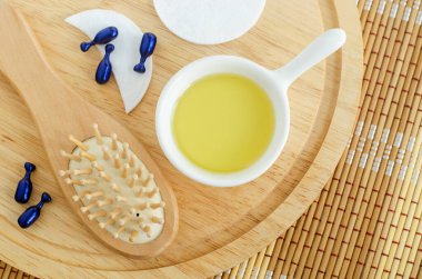 Küçük beyaz kase kozmetik (masaj, temizlik) yağı, yüz serumu kapsülleri ve ahşap saç fırçası. Doğal saç bakımı, spa ve güzellik tedavi tarifi. Üst görünüm, alanı kopyala. 