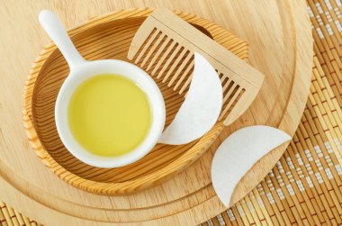 Kozmetik (masaj, temizlik) yağı, pamuk göz bandı ve ahşap saç fırçası ile küçük beyaz kase. Doğal saç bakımı, spa ve güzellik tedavi tarifi. Üst görünüm, alanı kopyala. 