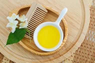 Kozmetik yağlı küçük beyaz kase, ahşap saç fırçası ve beyaz yasemin çiçekleri. Doğal saç bakımı, ev yapımı spa ve güzellik tedavi tarifi. Üst görünüm, alanı kopyala. 