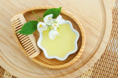 Kozmetik yağlı küçük beyaz kase, ahşap saç fırçası ve beyaz yasemin çiçekleri. Doğal saç bakımı, ev yapımı spa ve güzellik tedavi tarifi. Üst görünüm, alanı kopyala. 