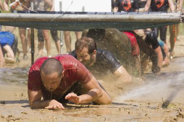 People passing  under the wires during the Inferno Run Mud Race