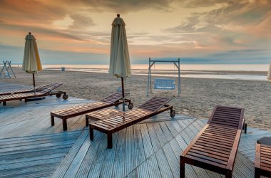 sandy beach at sea water, sunset sky, chairs, swing and umbrellas 
