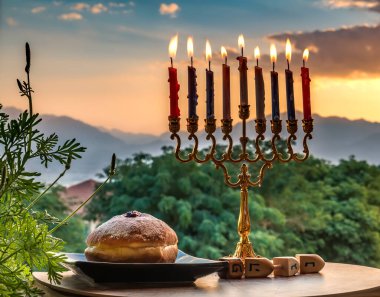 Mum yakmak, menorah ve Hanuka bayramı için ahşap dreidellerle donatılmış tatlı bir tabak - dreidel 'in yanında İbranice harfler - Büyük Mucize Burada Oldu. Bulanık park ve sabah gökyüzü dağlarla
