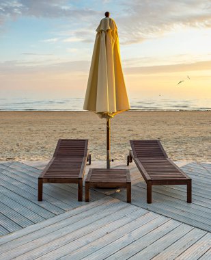 Güneş doğarken Baltık Denizi 'nin kumlu sahilinde boş iskemleler ve güneşlik.