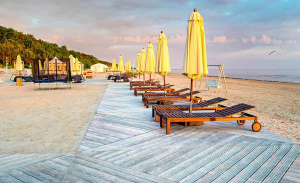 Şemsiyeleri, şezlongları ve ahşap zemini olan güzel kumlu plaj, turistik tatil beldesinde gün doğumu, Baltık Denizi, Avrupa