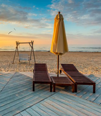 Baltık Denizi, Avrupa 'nın kumlu sahillerinde salıncak, güneşlik ve şezlonglarla dinlenme noktası. Renkli gün doğumu, yaz tatili konsepti ve iyi istirahatler.