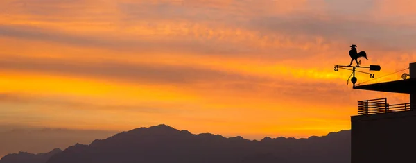 Renkli şafakta dekoratif metalik horozlu rüzgar gülü silueti. Şafak vakti renkli bulutlar ve güneş ışıkları. Hava tahmini kavramı 