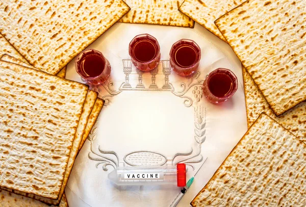 Pesah celebration concept - Jewish Passover holiday Unleavened bread food - matzoh and four glasses of red wine and medical tube with vaccine. White napkin with three Hebrew letters, in English translation mean Jewish Passover. Copy space for text