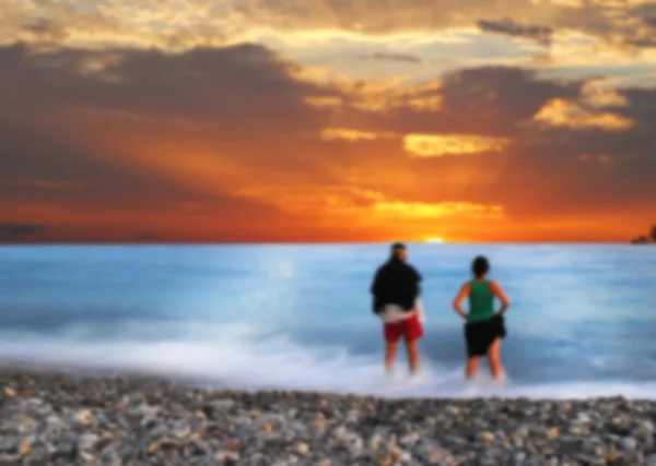 Bir erkek ve kadın gün batımında bakarak, dalgalar halinde ayakta — Stok fotoğraf