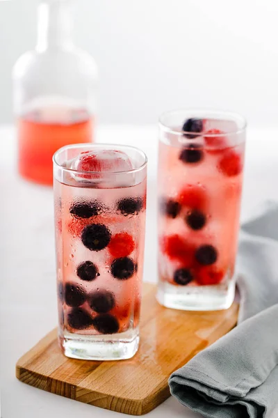 Two tall glasses of iced red fruits juice and distant bottle in the foreground